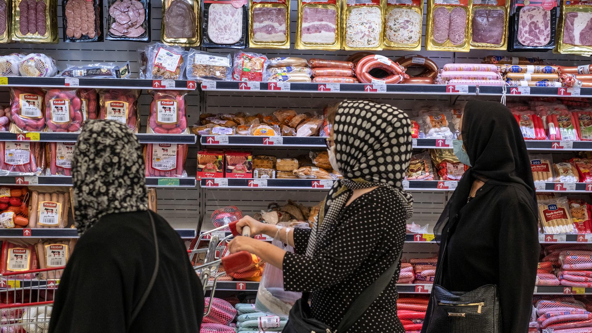 Frauen stehen vor einem mit Wurstwaren gefüllten Kühlregal in einem Supermarkt.