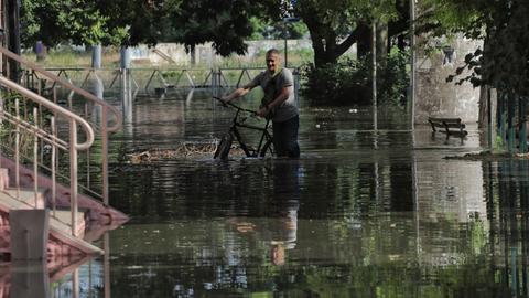 Ein Mann schiebt sein Fahrrad durch knietiefes Wasser.