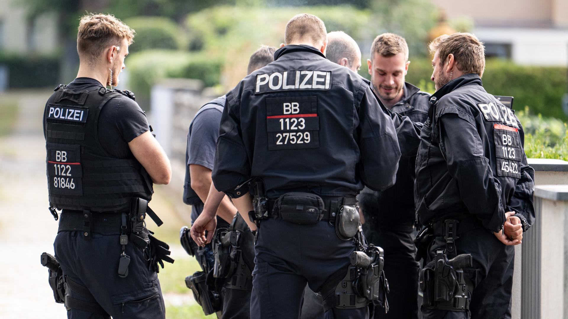 Mehrere Polizisten in blauen Uniformen stehen in einer Gruppe an einer Straße und beratschlagen. Mehrere Polizisten in blauen Uniformen stehen in einer Gruppe an einer Straße und beratschlagen.