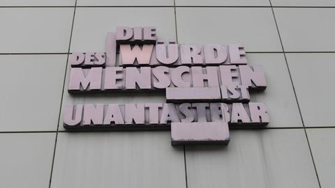 Der Schriftzug "Die Würde des Menschen ist unantastbar" steht in Großbuchstaben aus Metall an einem Gerichtsgebäude in Frankfurt am Main.