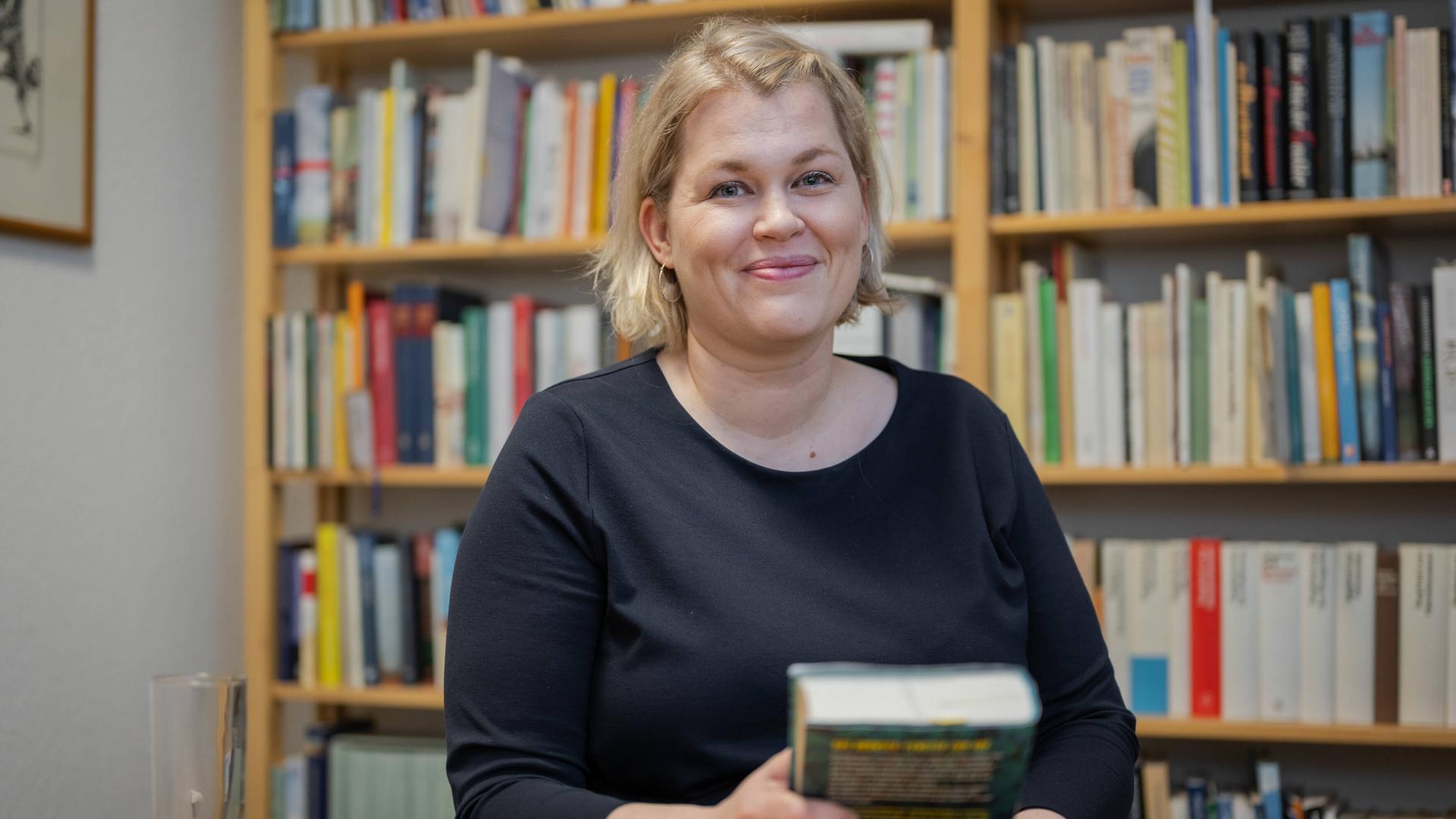 Die Schriftstellerin Berit Glanz zu Gast im Literaturhaus Schleswig-Holstein in Kiel. Sie lächelt in die Kamera, sitzt hinter einem Schreibtisch und hält ein Buch in der Hand. Im Hintergrund sind Bücherregale zu erkennen. Die Schriftstellerin Berit Glanz zu Gast im Literaturhaus Schleswig-Holstein in Kiel. Sie lächelt in die Kamera, sitzt hinter einem Schreibtisch und hält ein Buch in der Hand. Im Hintergrund sind Bücherregale zu erkennen.