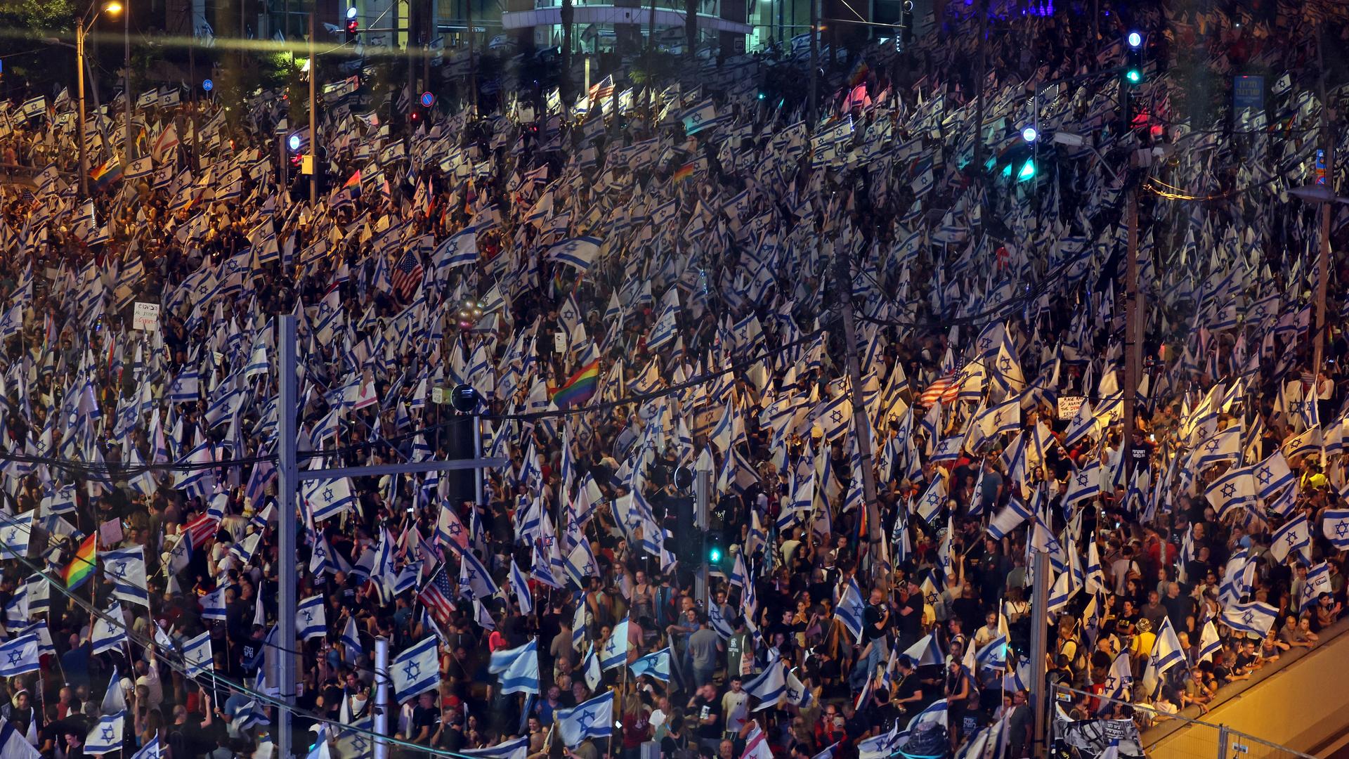 In Tel Aviv sind in der Dunkelheit tausende Menschen auf der Straße zu sehen. Viele tragen israelische Flaggen. In Tel Aviv sind in der Dunkelheit tausende Menschen auf der Straße zu sehen. Viele tragen israelische Flaggen.