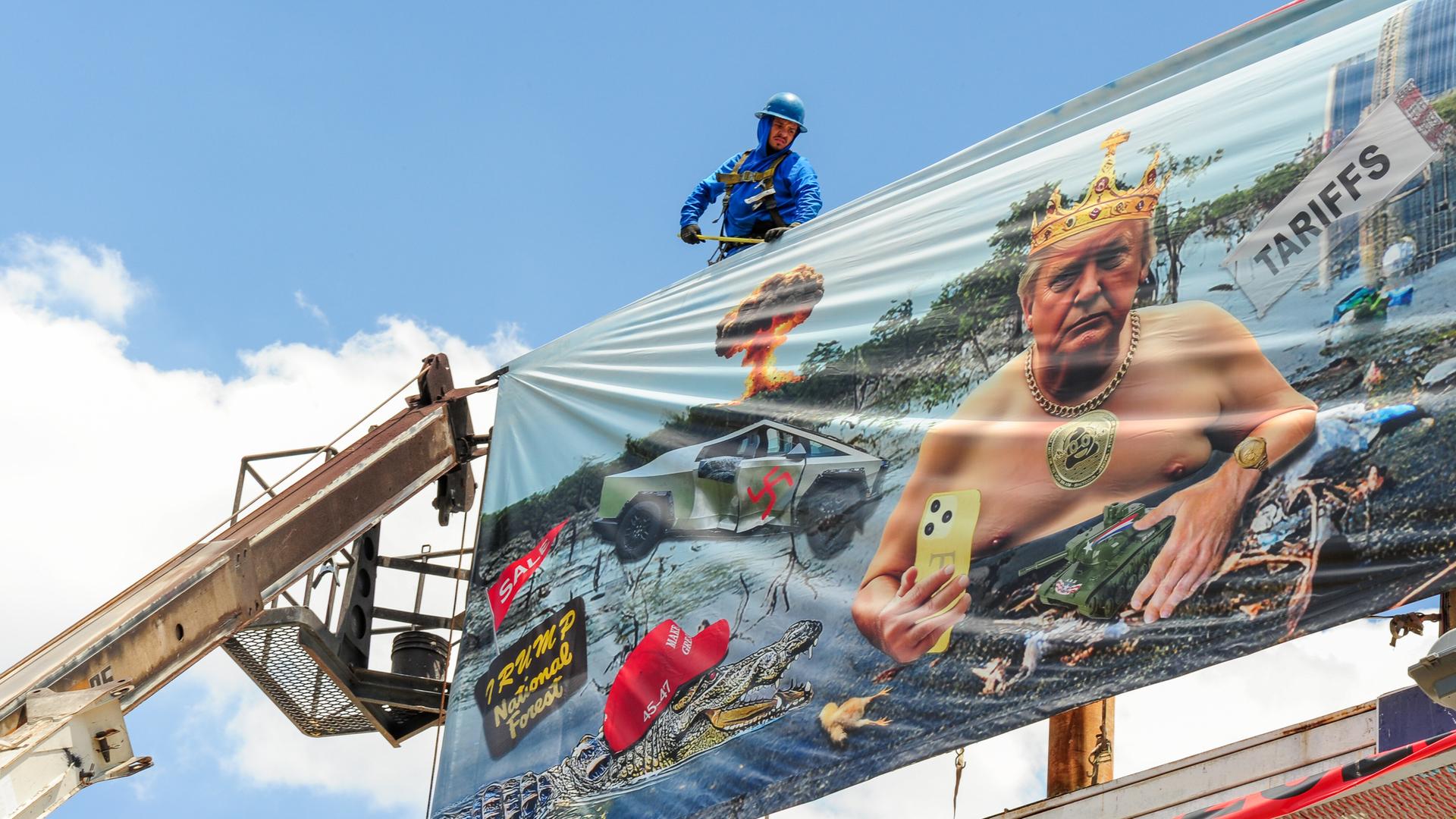 Arbeiter installieren eine Plakatwand der Künstlerin Karen Fiorito in Phoenix. Das Werk mit dem Titel „Swamp King“ kritisiert Donald Trumps Präsidentschaft mit Bildern, die Korruption, Autoritarismus und systemischen Verfall symbolisieren. 