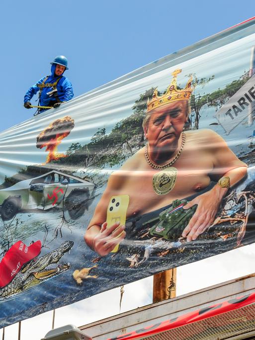 Arbeiter installieren eine Plakatwand der Künstlerin Karen Fiorito in Phoenix. Das Werk mit dem Titel „Swamp King“ kritisiert Donald Trumps Präsidentschaft mit Bildern, die Korruption, Autoritarismus und systemischen Verfall symbolisieren. 
