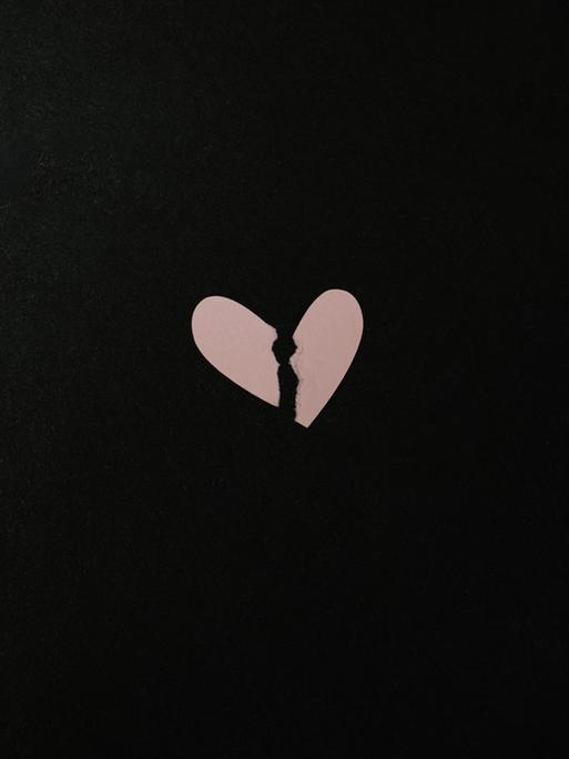 Ein gebrochenes Herz aus Papier vor schwarzem Hintergrund
