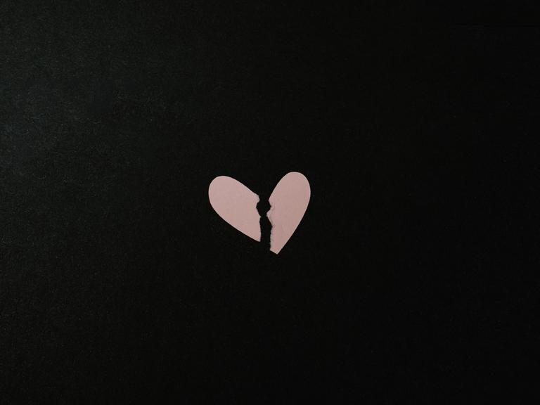 Ein gebrochenes Herz aus Papier vor schwarzem Hintergrund