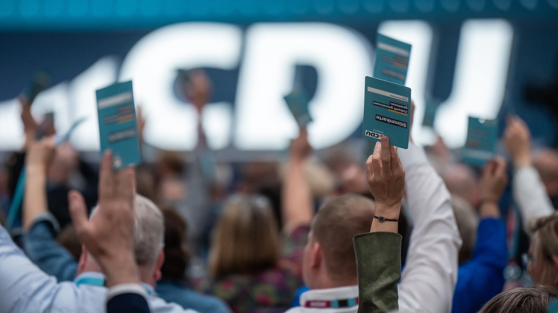 Delegierte der CDU halten bei einer Abstimmung Stimmkarten in die Höhe.