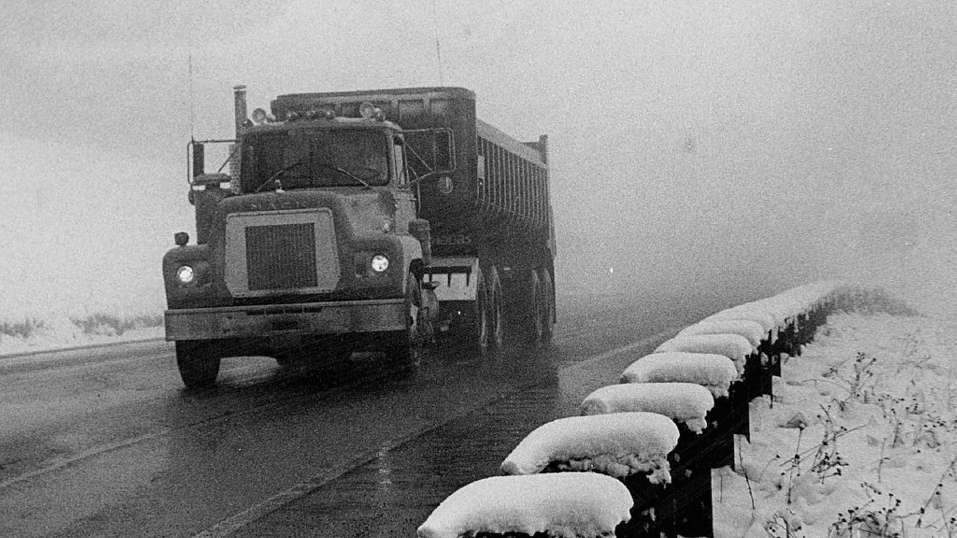 Schwarz-Weiß-Bild eines alten LKWs auf einer Straße bei Schneewetter.