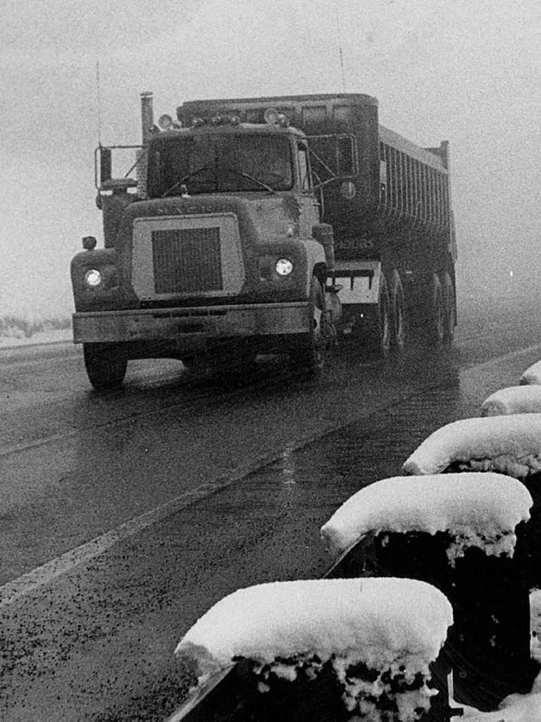 Schwarz-Weiß-Bild eines alten LKWs auf einer Straße bei Schneewetter.
