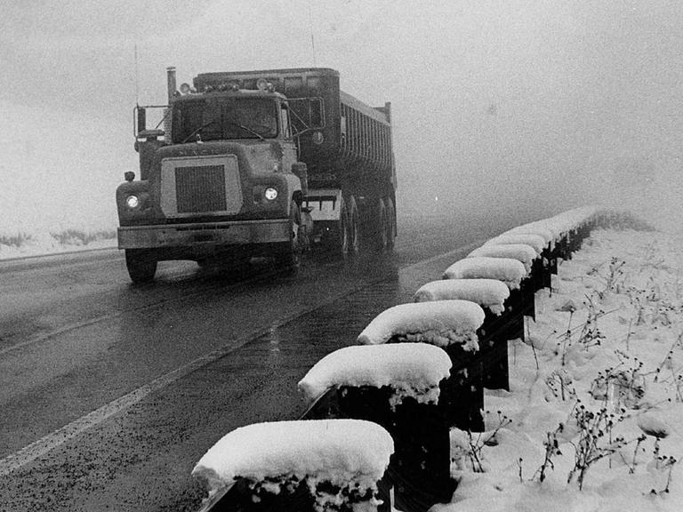 Schwarz-Weiß-Bild eines alten LKWs auf einer Straße bei Schneewetter. Schwarz-Weiß-Bild eines alten LKWs auf einer Straße bei Schneewetter.