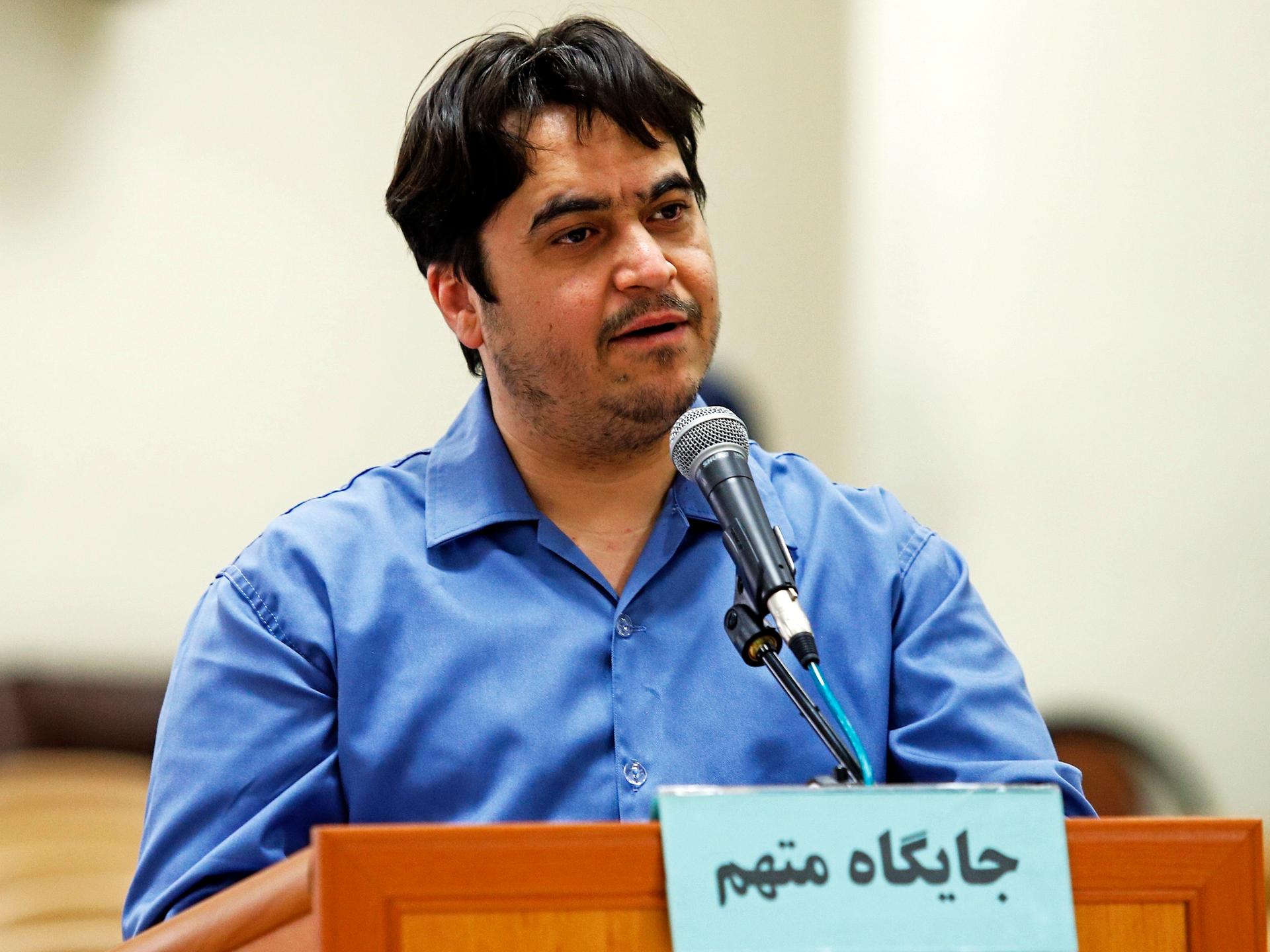 Der Journalist Ruhollah Zam steht in einem blauen Hemd hinter einem Holzpult.