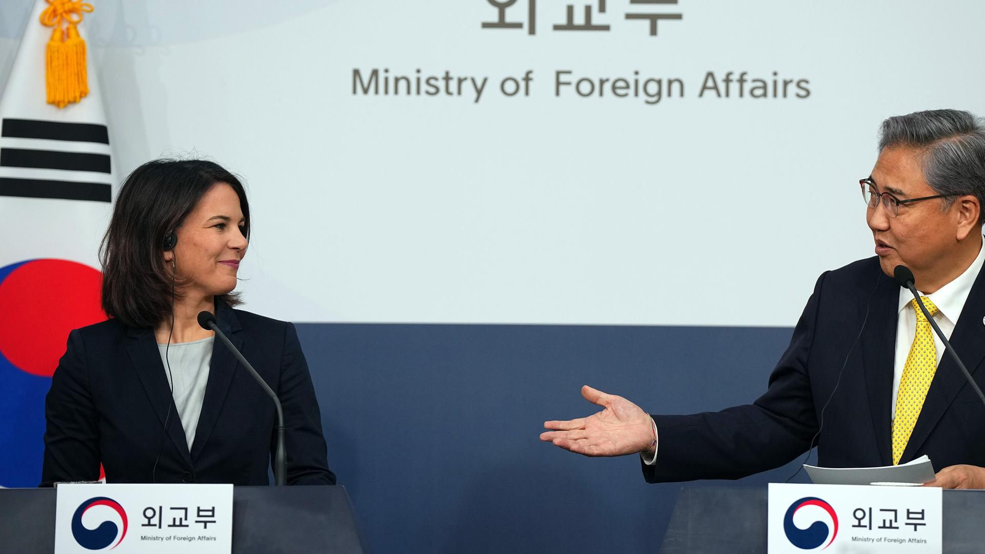Annalena Baerbock und der südkoreanische Außenminister Park Jin stehen hinter Rednerpunlten und lächeln: Park macht eine einladende Handbewegung.