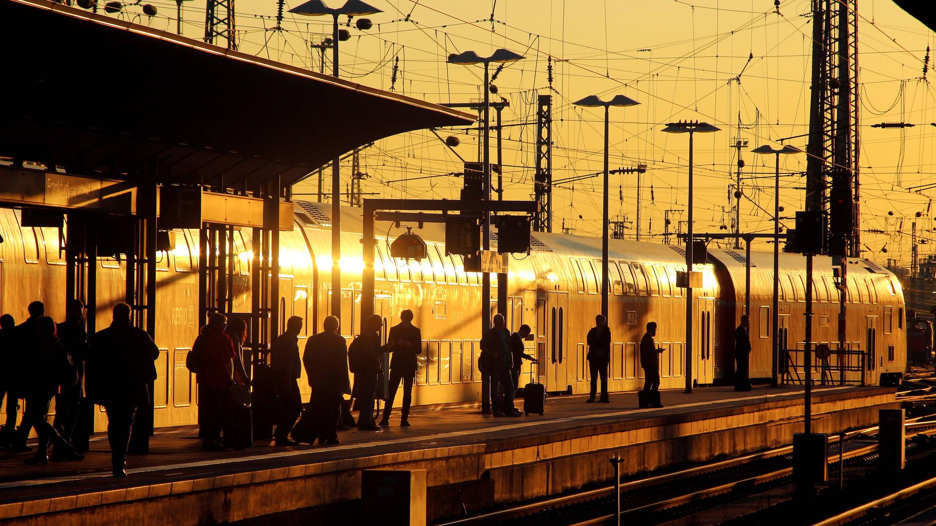 Fahrgäste auf einem Bahnsteig mit einem einfahrenden Nahverkehrszug der Deutschen Bahn in der Abendsonne am Hauptbahnhof in Frankfurt am Main.
