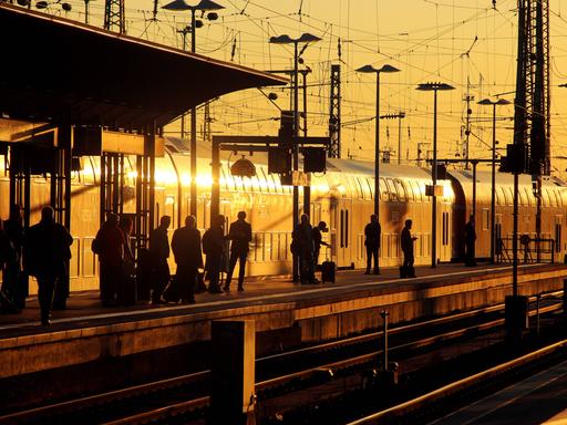 Fahrgäste auf einem Bahnsteig mit einem einfahrenden Nahverkehrszug der Deutschen Bahn in der Abendsonne am Hauptbahnhof in Frankfurt am Main.