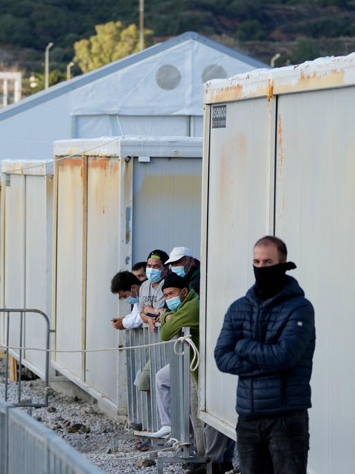 Flüchtlingslager auf der griechischen Insel Lesbos am 5. Dezember 2021. Blick an einer Container-Hausfront entlang, mehrere Flüchtlinge stehen wartend am Rand.