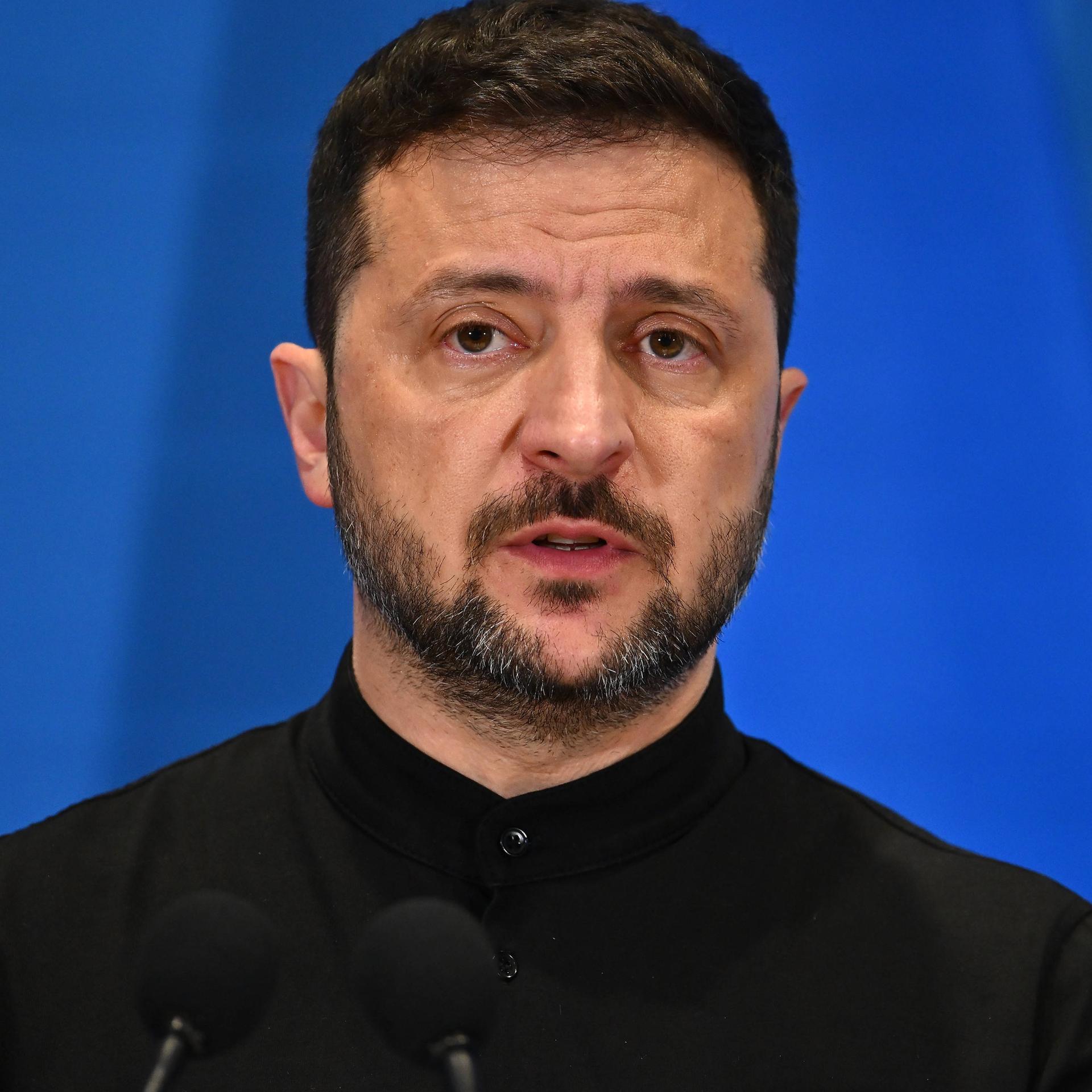 Wolodymyr Selenskyj steht auf einem Podium vor blauem Hintergrund.
