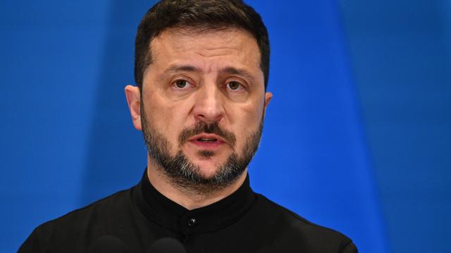 Wolodymyr Selenskyj steht auf einem Podium vor blauem Hintergrund.