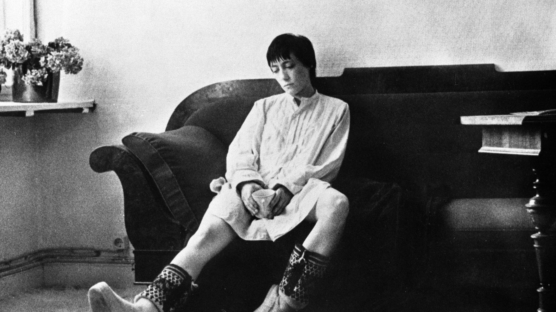Das Schwarz-weiß-Bild zeigt eine junge Frau mit kurzen dunklen Haaren, die auf einem Sofa sitzt.