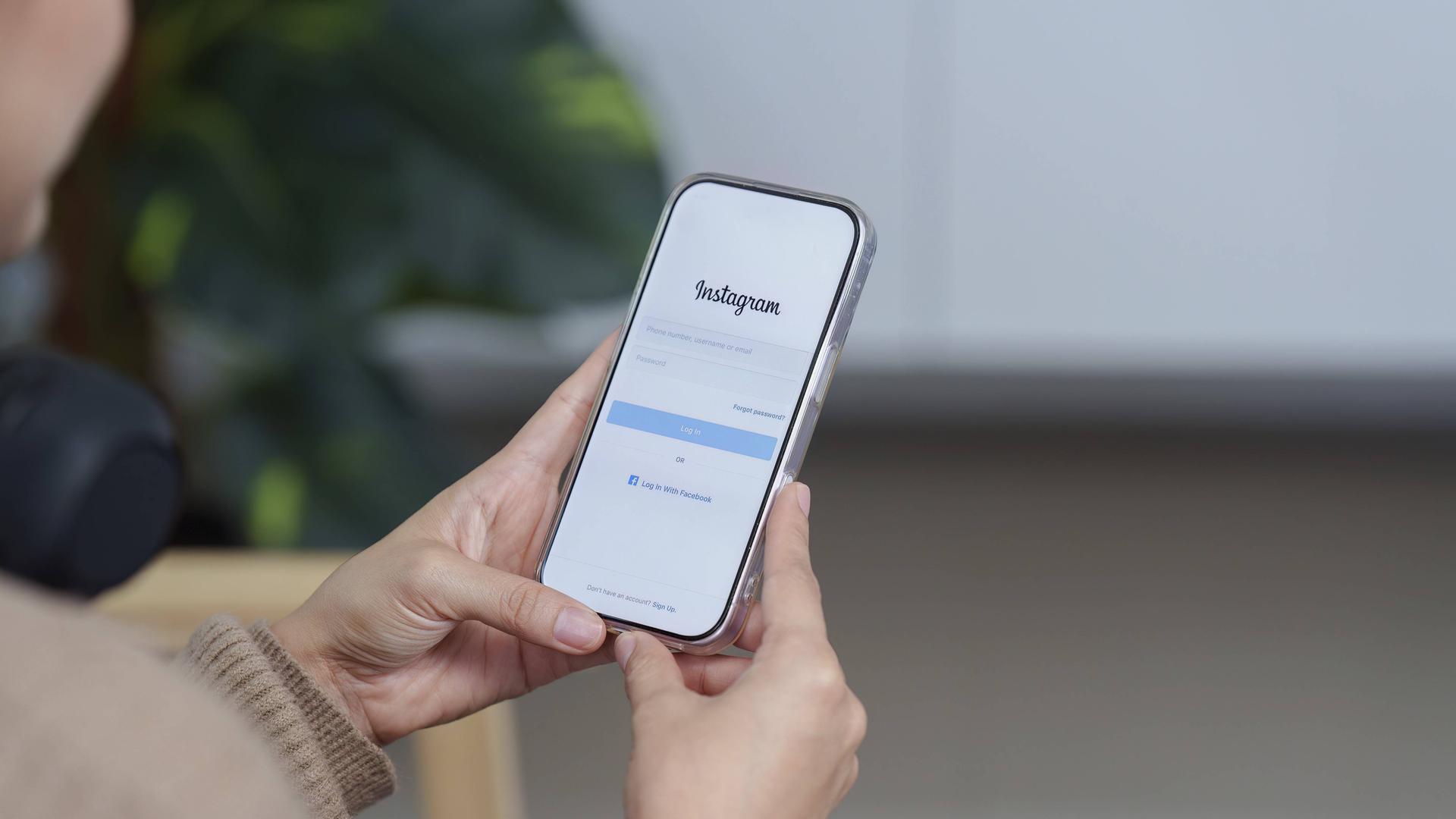Eine Frau hält ein Samrtphone in der Hand, auf dem der Anmeldebildschirm von Instagram zu sehen ist. Eine Frau hält ein Samrtphone in der Hand, auf dem der Anmeldebildschirm von Instagram zu sehen ist.