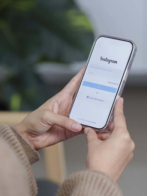 Eine Frau hält ein Samrtphone in der Hand, auf dem der Anmeldebildschirm von Instagram zu sehen ist.