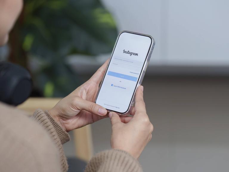 Eine Frau hält ein Samrtphone in der Hand, auf dem der Anmeldebildschirm von Instagram zu sehen ist.