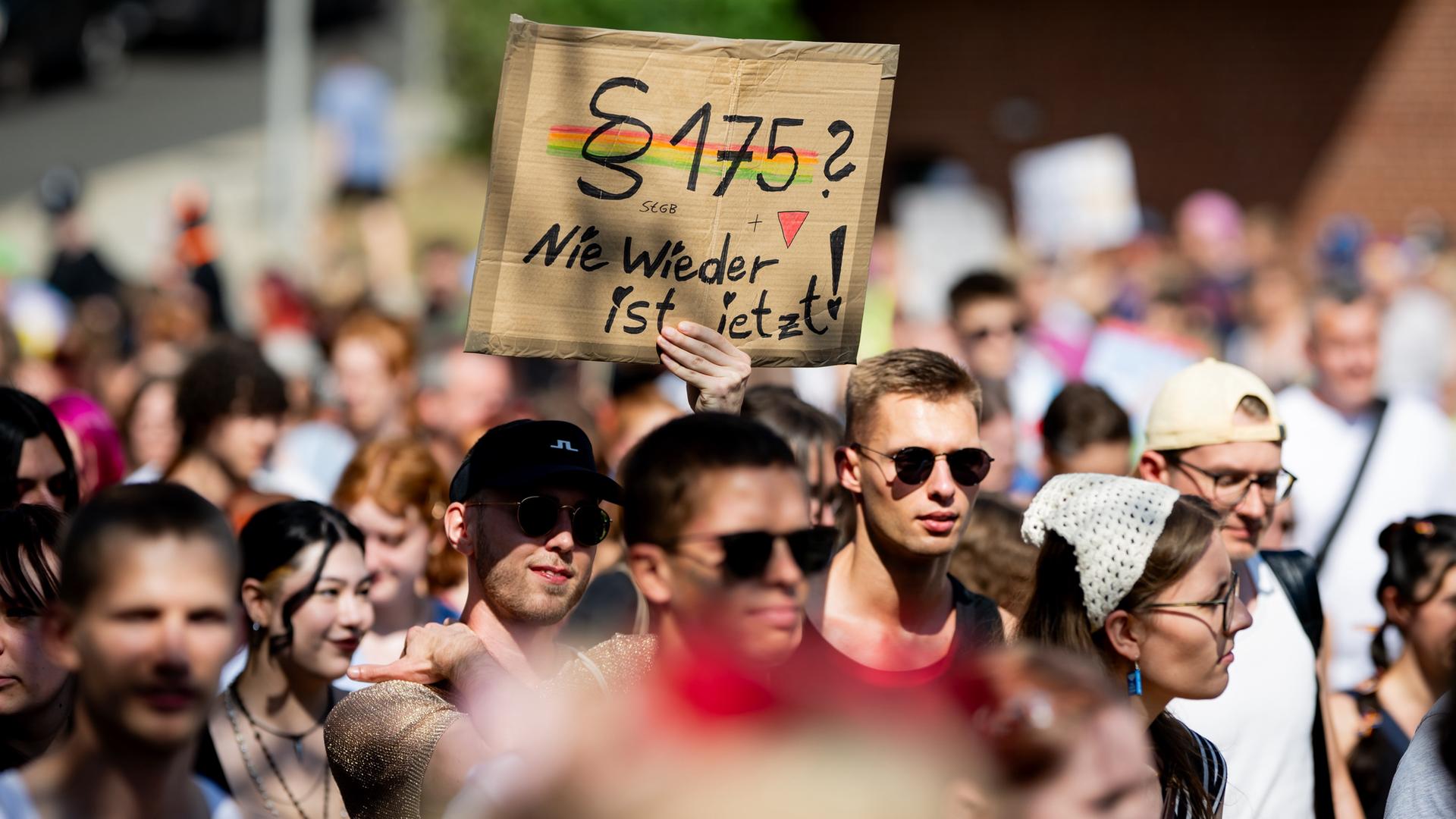 Ein Teilnehmer in einer Menschenmenge hält ein Schild mit der Aufschrift "Â§175? Nie wieder ist jetzt!" hoch.