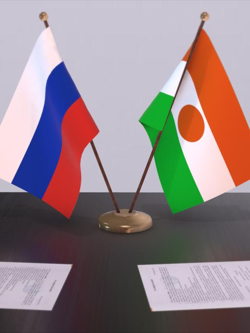 Die Nationalflaggen Russlands und Nigers stehen auf einem Tisch nebeneinander. 