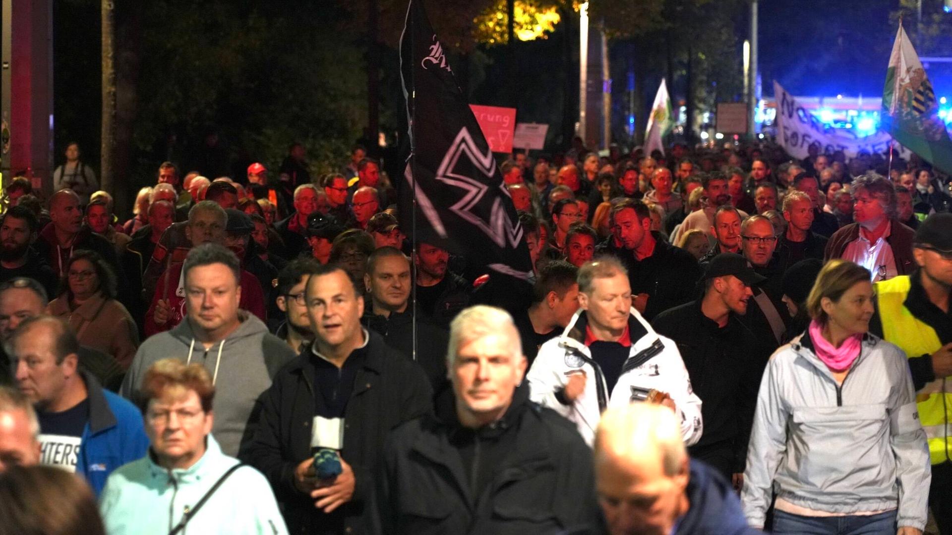 Viele Menschen demonstrieren auf einer Straße, in der Mitte ist eine alte Reichskriegsflagge mit schwarzem Kreuz zu sehen.