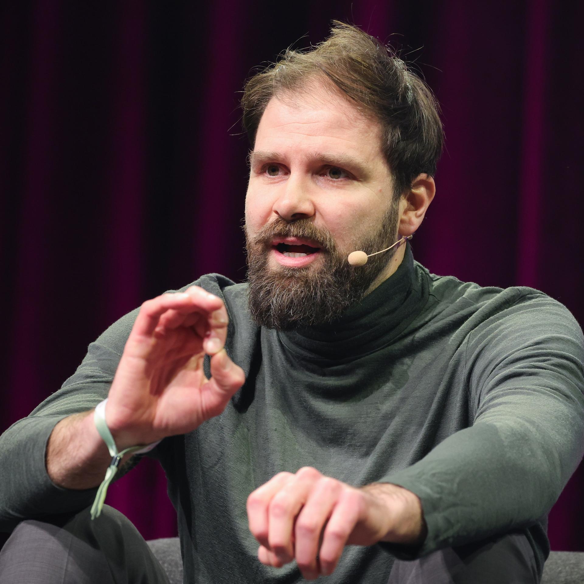 Johannes Herber, Geschäftsführer Interessengemeinschaft Athleten Deutschland, sitzt bei einem Podiumsgespräch auf der Bühne und gestikuliert mit den Händen. 