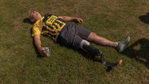 Ein ukrainischer Veteran mit einer Beinprothese liegt nach einem Rennen in seiner Sportkleidung flach auf dem Rasen, um auszuruhen.