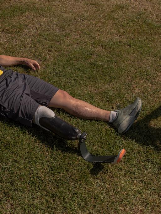 Ein ukrainischer Veteran mit einer Beinprothese liegt nach einem Rennen in seiner Sportkleidung flach auf dem Rasen, um auszuruhen.
