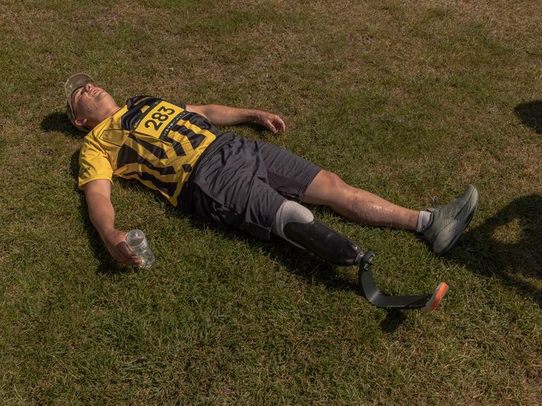 Ein ukrainischer Veteran mit einer Beinprothese liegt nach einem Rennen in seiner Sportkleidung flach auf dem Rasen, um auszuruhen.