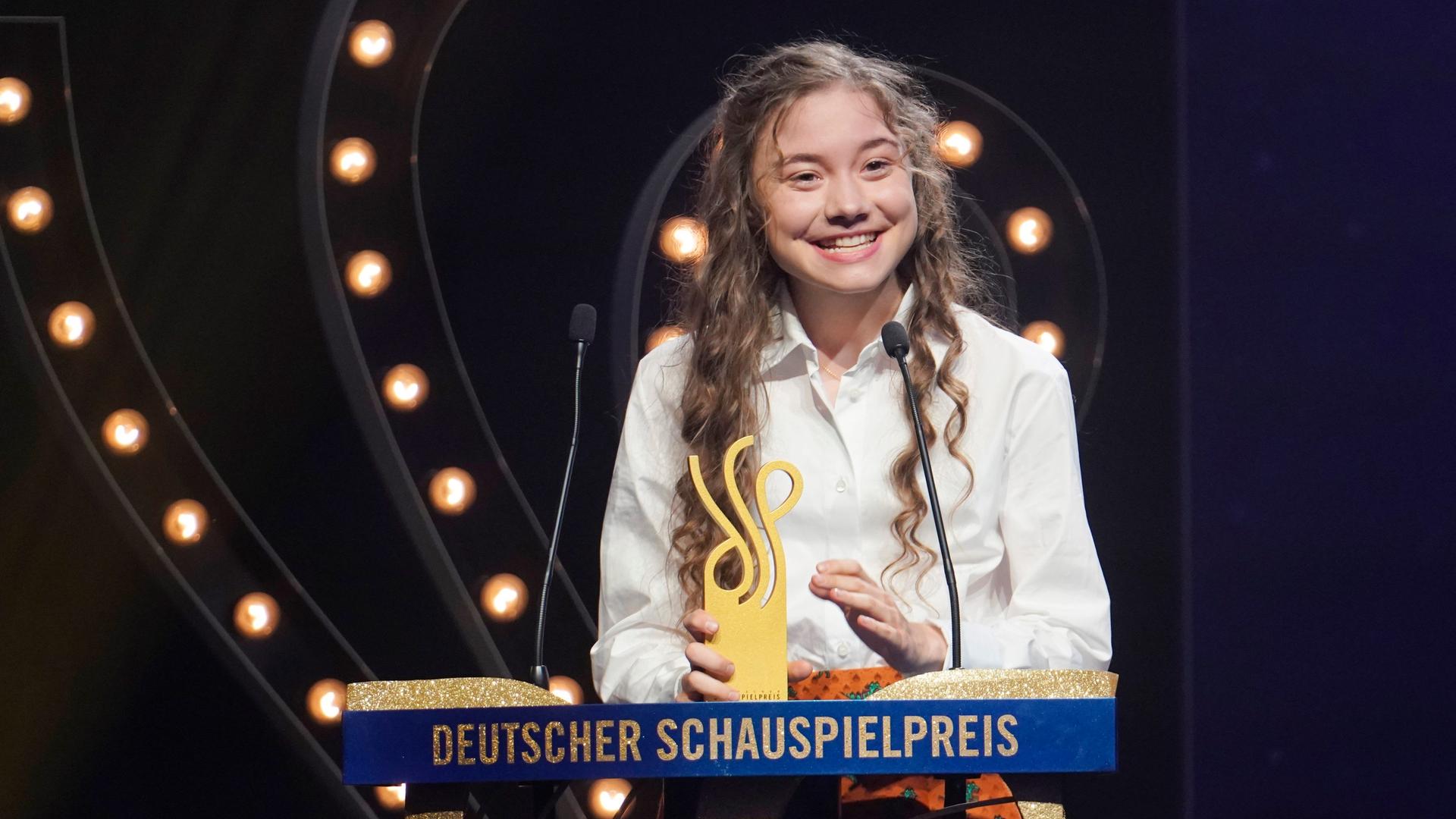 Hannah Schiller steht lachend am Rednerpult beim Deutschen Schauspielpreis. Neben ihr steht der Preis, mit dem sie ausgezeichnet wurde.