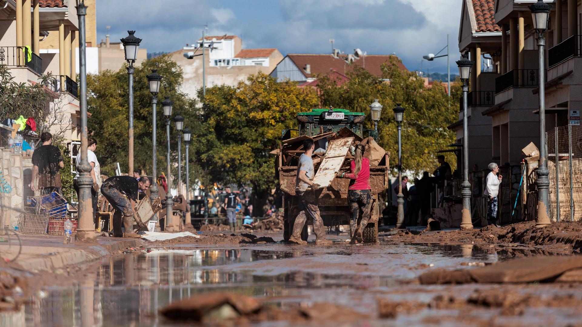 Menschen beladen einen Lastwagen mit Sperrmüll auf einer Straße voller Schlamm in Valencia. 