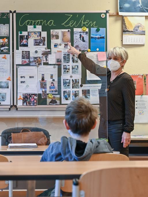 Die Lehrerin einer 4. Klasse an der Grundschule "Am Mühlenfließ" in Frankfurt (Oder), unterrichtet zwei SchülerInnen in einem Klassenzimmer. Auf der Tafal steht "Lernen in Corona Zeiten".