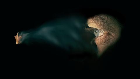 Spion: Ein kleines Loch in der Wand wirft Licht auf ein Auge hinter der Wand.