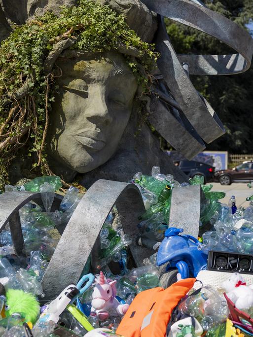 Vor dem UN-Hauptsitz in Genf steht eine sechs Meter hohe Skulptur von Benjamin Von Wong: eine Neuinterpretation von Rodins „Denker“, beladen mit gesammelten Plastikteilen. Im Vordergrund liegen weitere Plastikgegenstände.