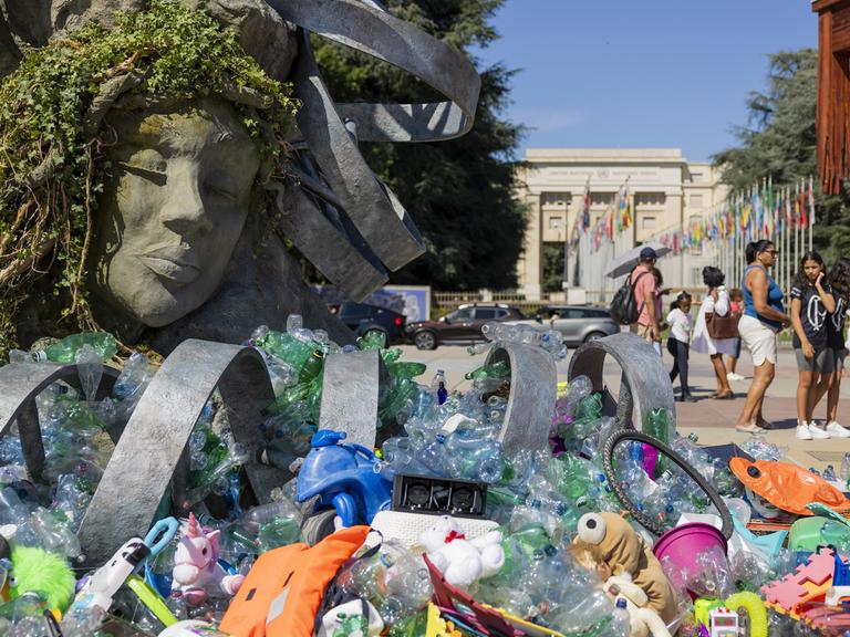 Vor dem UN-Hauptsitz in Genf steht eine sechs Meter hohe Skulptur von Benjamin Von Wong: eine Neuinterpretation von Rodins „Denker“, beladen mit gesammelten Plastikteilen. Im Vordergrund liegen weitere Plastikgegenstände.