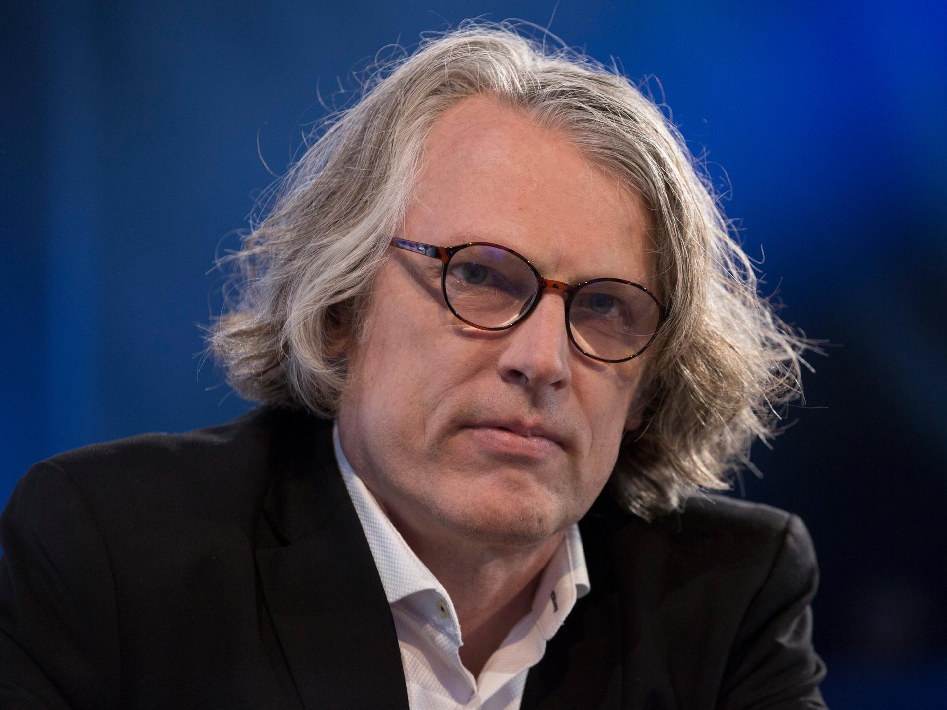 Peter Trawny auf der Buchmesse. Er hat mittellanges graues Haar, trägt eine Brille und ein weißes Hemd zum dunklen Anzug.