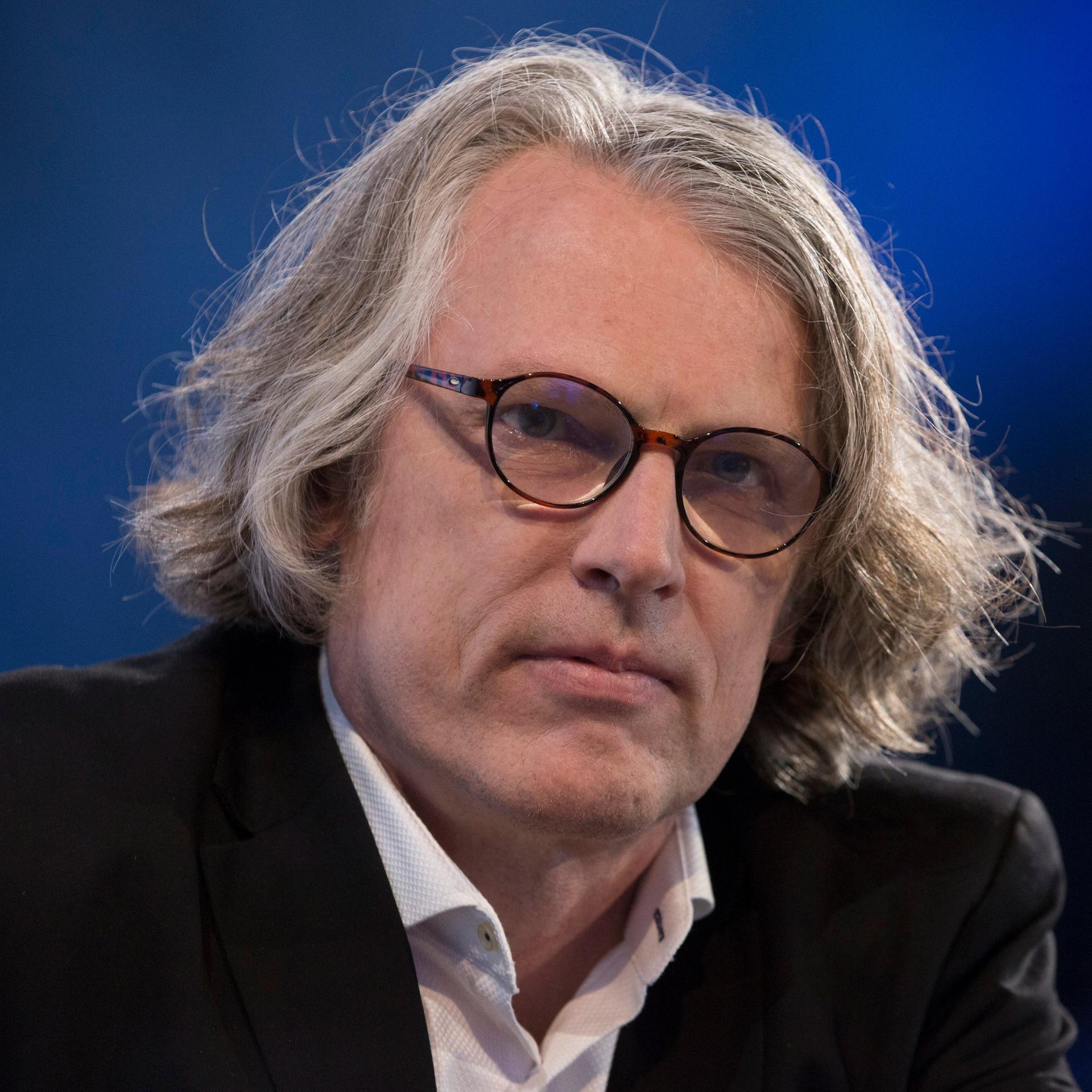 Peter Trawny auf der Buchmesse. Er hat mittellanges graues Haar, trägt eine Brille und ein weißes Hemd zum dunklen Anzug.