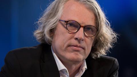 Peter Trawny auf der Buchmesse. Er hat mittellanges graues Haar, trägt eine Brille und ein weißes Hemd zum dunklen Anzug.