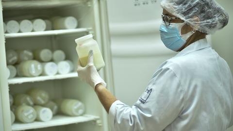 Eine Krankenschwester ordnet Flaschen mit Muttermilch in einem Kühlschrank. Sie trägt einen Haarschutz und einen Mund-Nasen-Schutz.