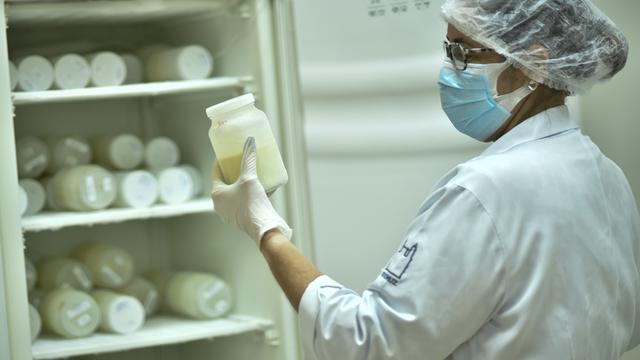 Eine Krankenschwester ordnet Flaschen mit Muttermilch in einem Kühlschrank. Sie trägt einen Haarschutz und einen Mund-Nasen-Schutz.