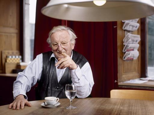 Peter Bichsel sitzt am Tisch und zeigt in die Kamera