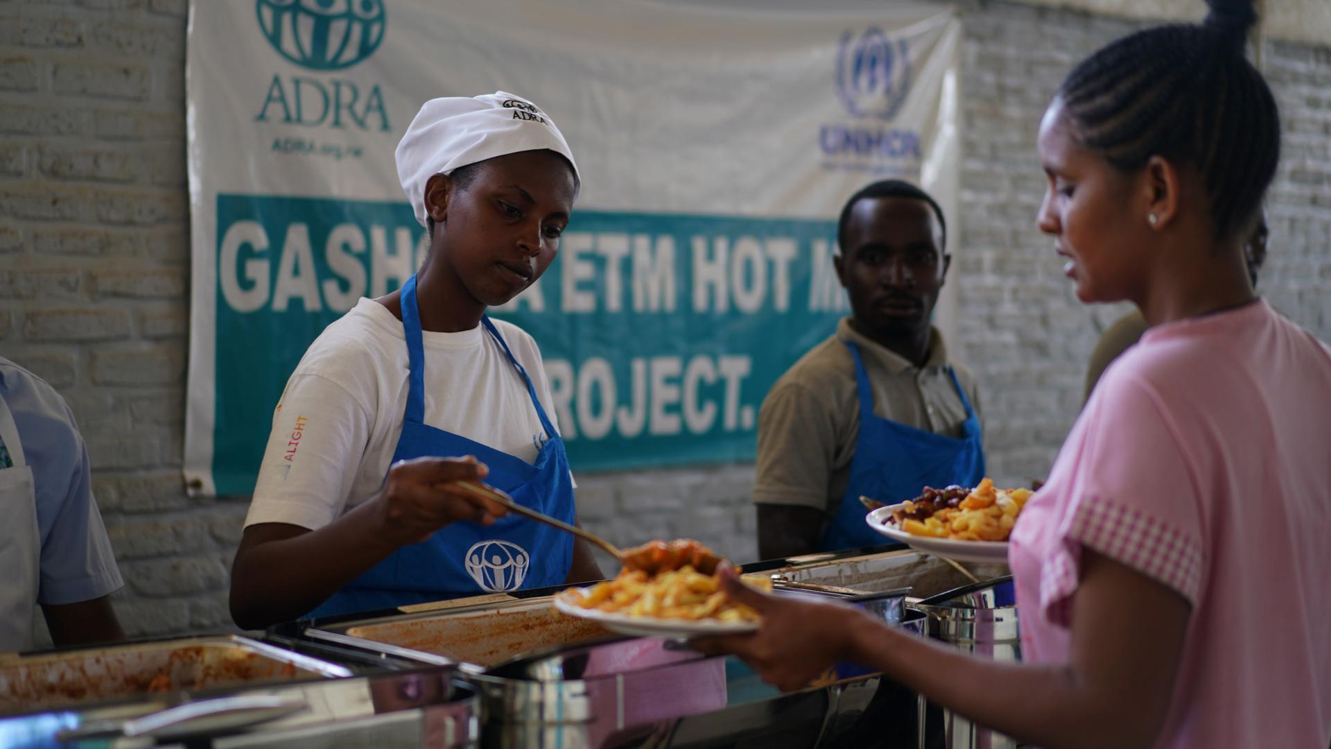 Eine Küchenhilfe tut an einem Tresen anstehenden Menschen Essen auf: im Flüchtlingscamp Gashora in Ruanda. Eine Küchenhilfe tut an einem Tresen anstehenden Menschen Essen auf: im Flüchtlingscamp Gashora in Ruanda.