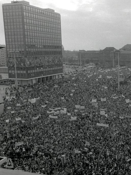 Auf dem Berliner Alexanderplatz ist eine große Menschenmenge mit Transparenten versammelt.