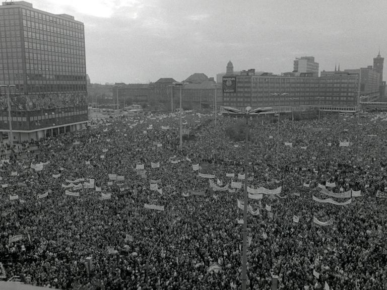 Auf dem Berliner Alexanderplatz ist eine große Menschenmenge mit Transparenten versammelt.