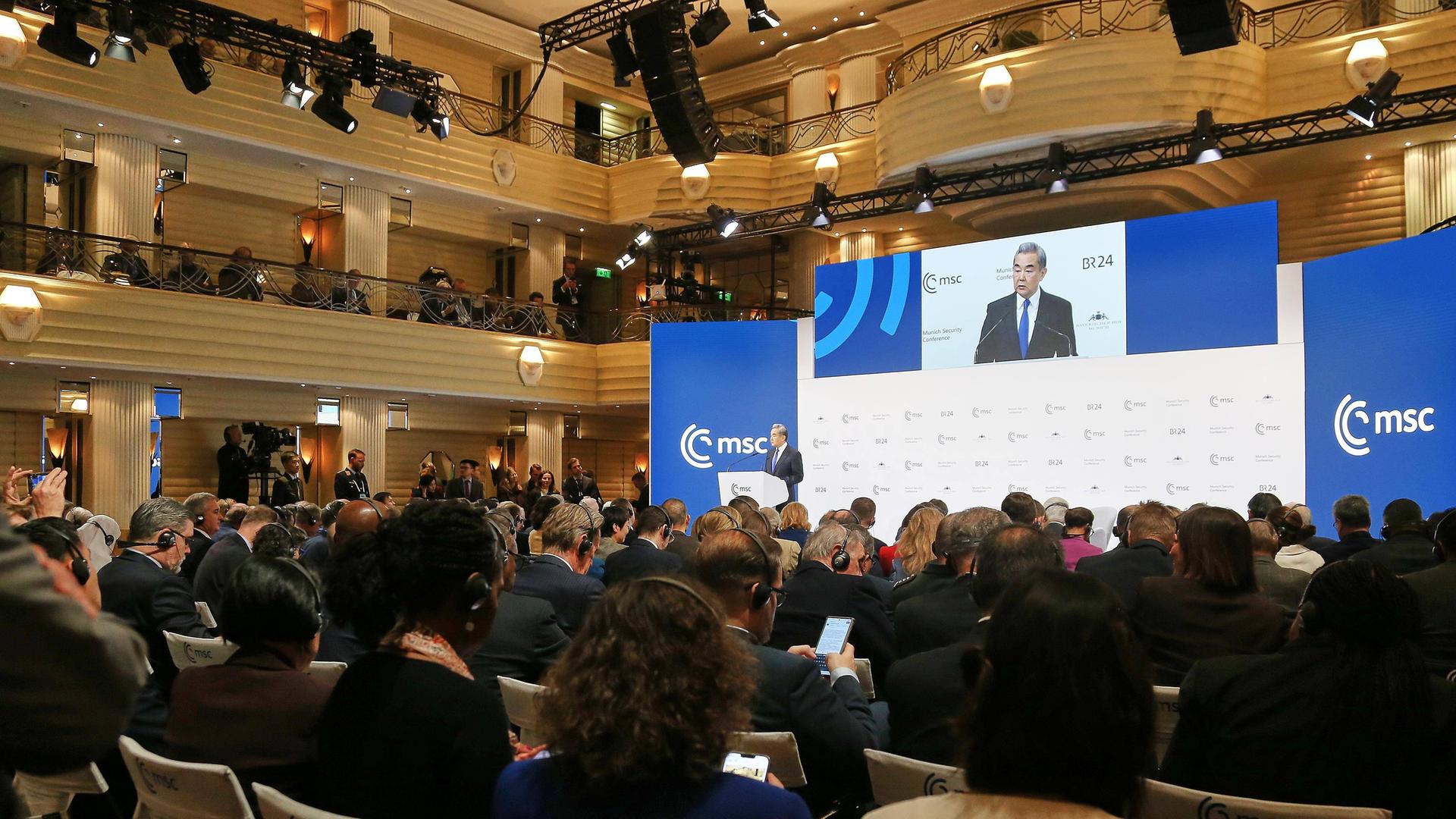 Blick in den Saal der Münchner Sicherheitskonferenz, wo der chinesische Außenminster Wang Yi auf einer großen Leinwand zu sehen ist. 