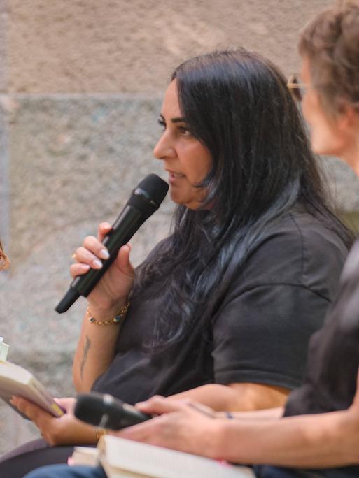 Die Töchter ermordeter Terroropfer, Semiya Şimşek und Gamze Kubaşık, halten Mikros in der Hand, eine von spricht, während sie ein Buch in der Hand hält.