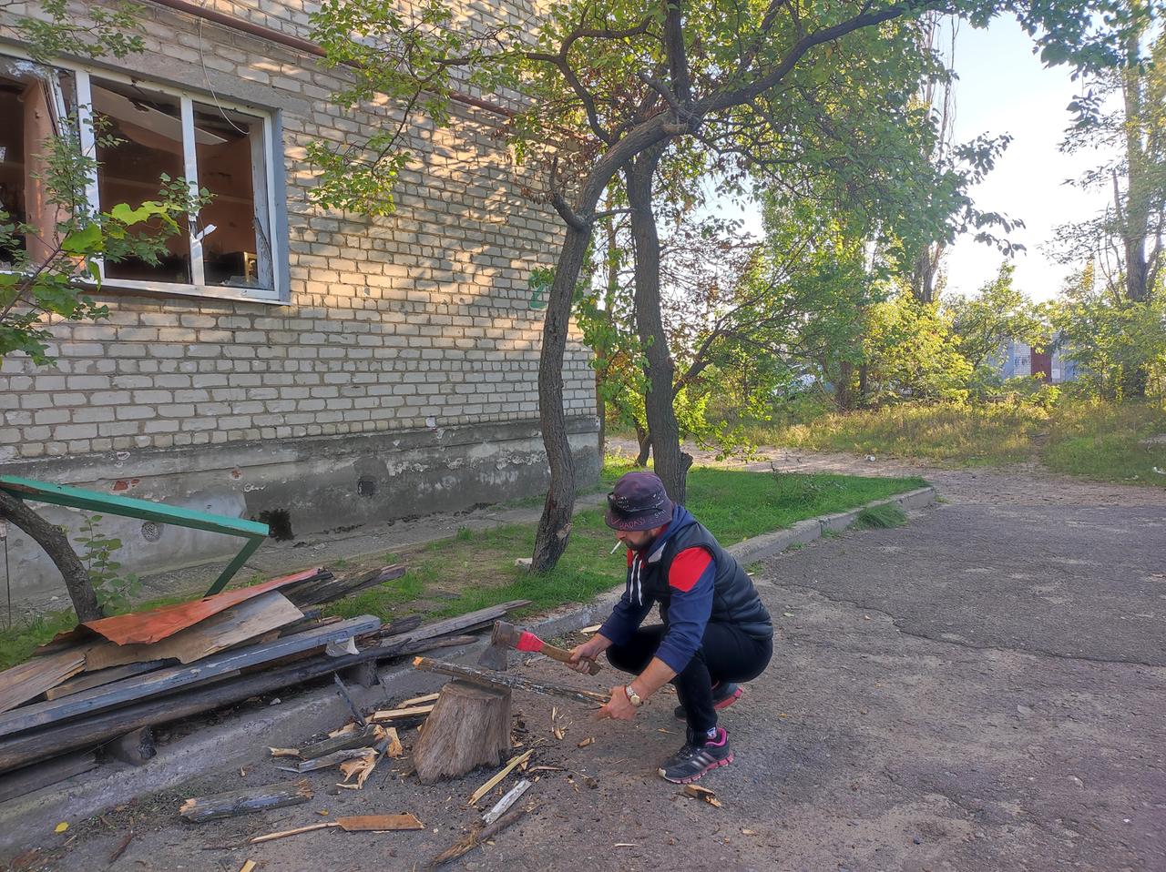 Der Ukrainer Maksim Surschan. Ein Mann hockt vor einem Haus und hackt Holz.
